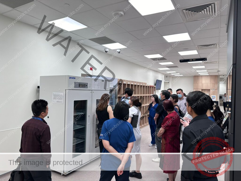 A group of people stand in a room, observing a large piece of equipment in a lab or medical setting.