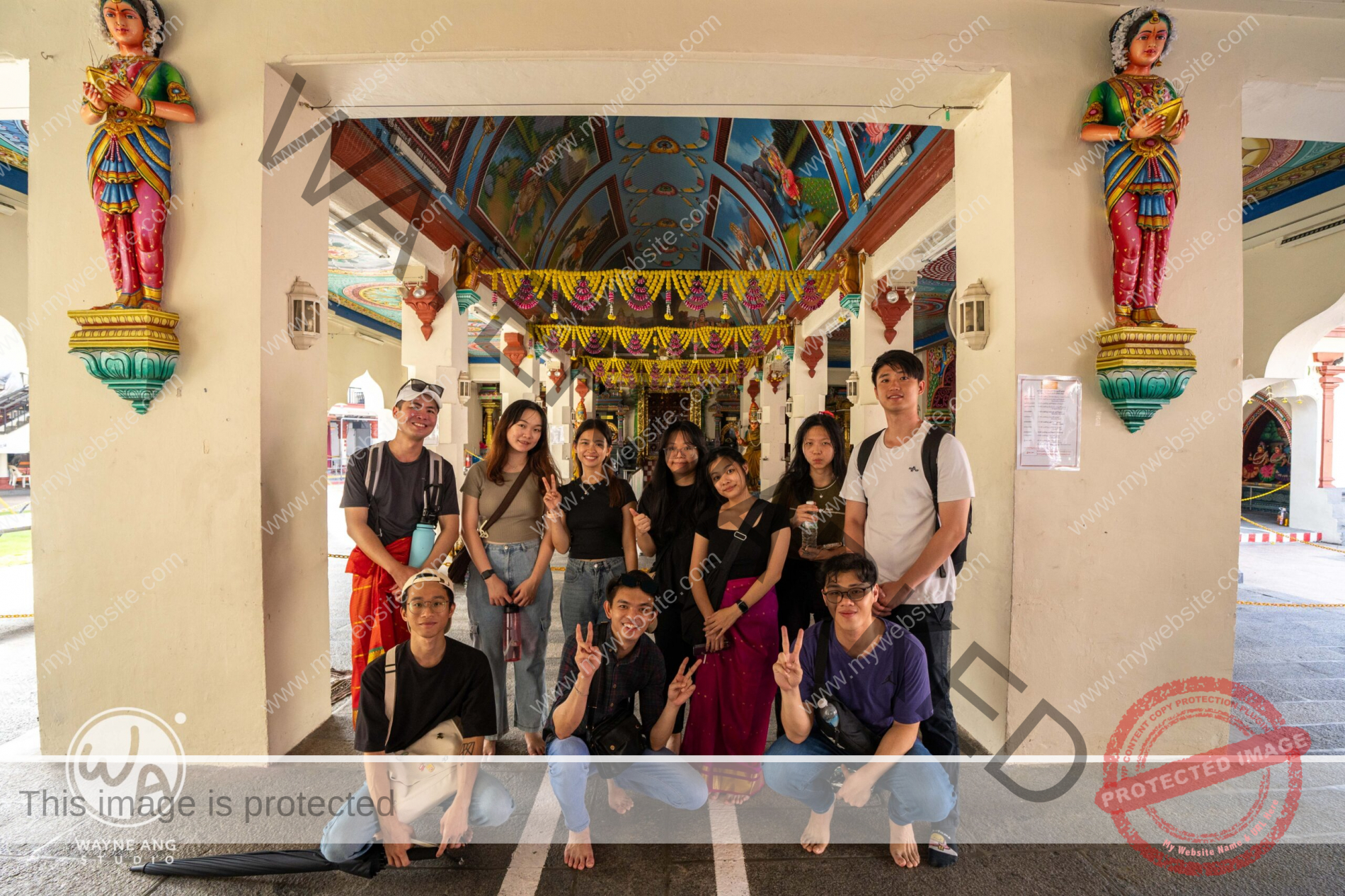 A group of people pose barefoot for a photo inside a vibrantly decorated temple with colorful statues and painted ceiling, capturing a memorable moment from their leadership development camp.