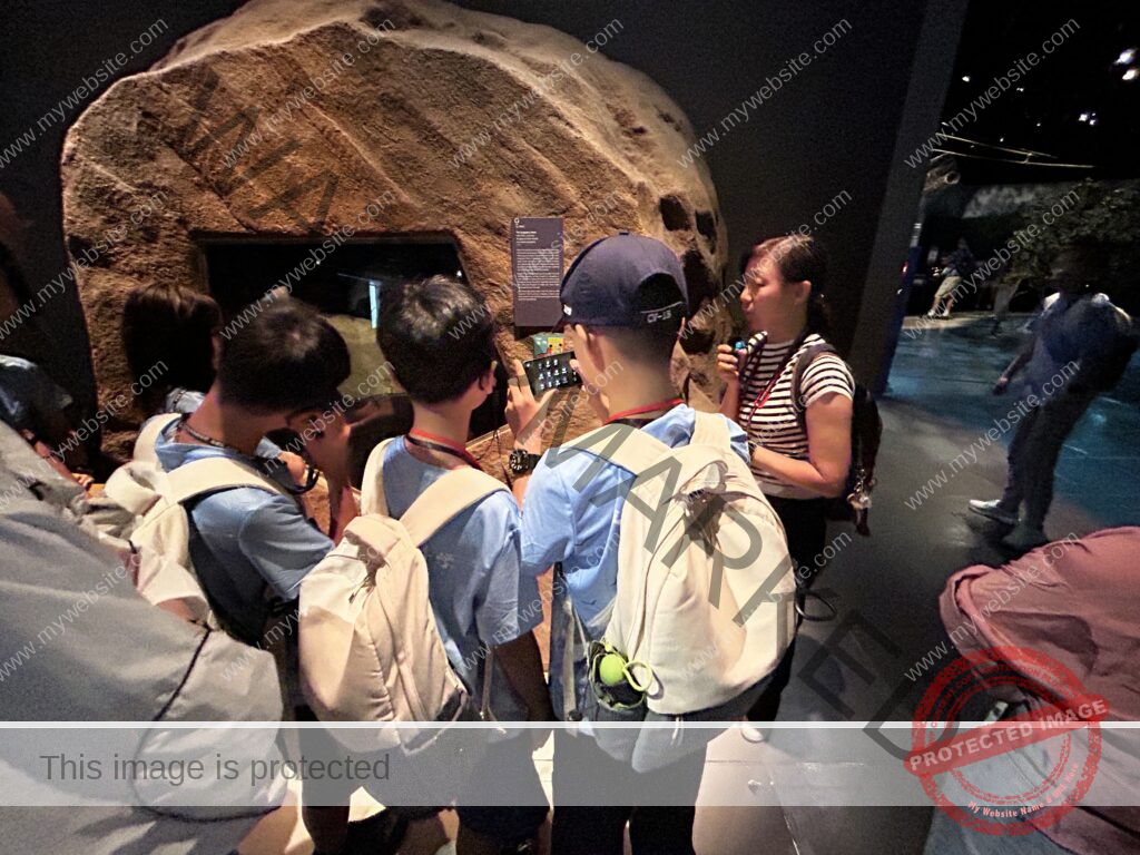 Our students with backpacks listen attentively as a guide explains an exhibit at a museum, embracing outdoor learning in Singapore.